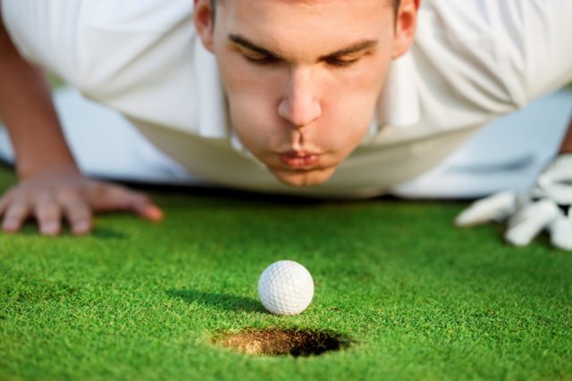 Golfer blowing ball into hole